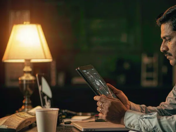 p88 Man studying a match-data interface on a tablet beside a cricket bat and coffee