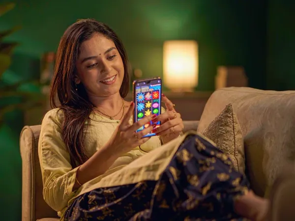 p88 Woman relaxing on a plush sofa, smiling at a smartphone showing a colourful slot game