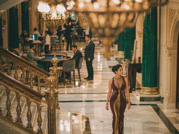 p88 Woman in a maroon and gold dress walking through a chandelier-lit casino lobby